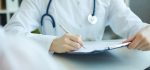 A doctor in a white lab coat with a stethoscope writing on a chart.