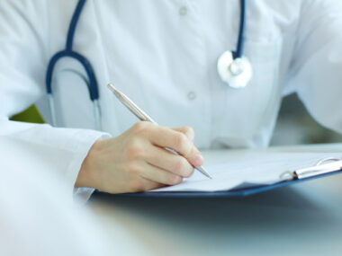 A doctor in a white lab coat with a stethoscope writing on a chart.
