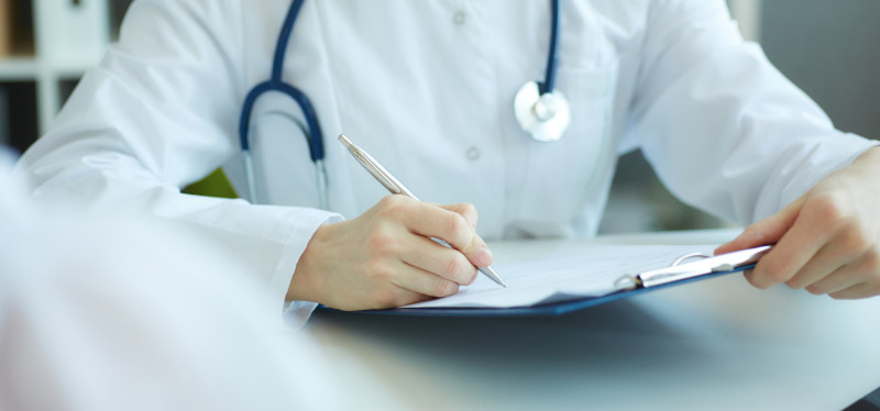 A doctor in a white lab coat with a stethoscope writing on a chart.