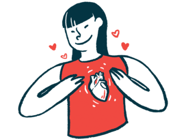A woman smiles while gesturing to an heart pictured on her shirt.