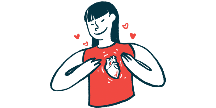 A woman smiles while gesturing to an heart pictured on her shirt.
