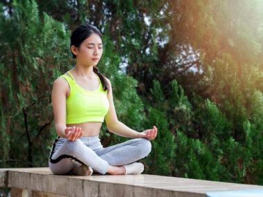 a woman in sportswear practicing meditation while sitting in the lotus position on a wall